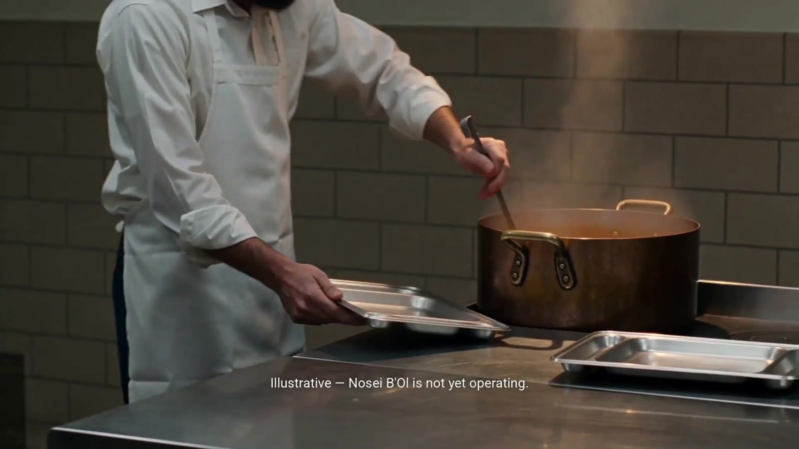 A volunteer ladling hot food onto trays in a stainless-steel kitchen
